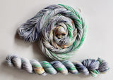 A swirl of yarn sits above a twisted hank on a clean white background.