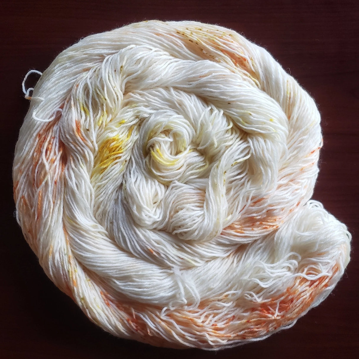 A bright swirl of yarn curls around itself like a labyrinth against a dark maroon background.