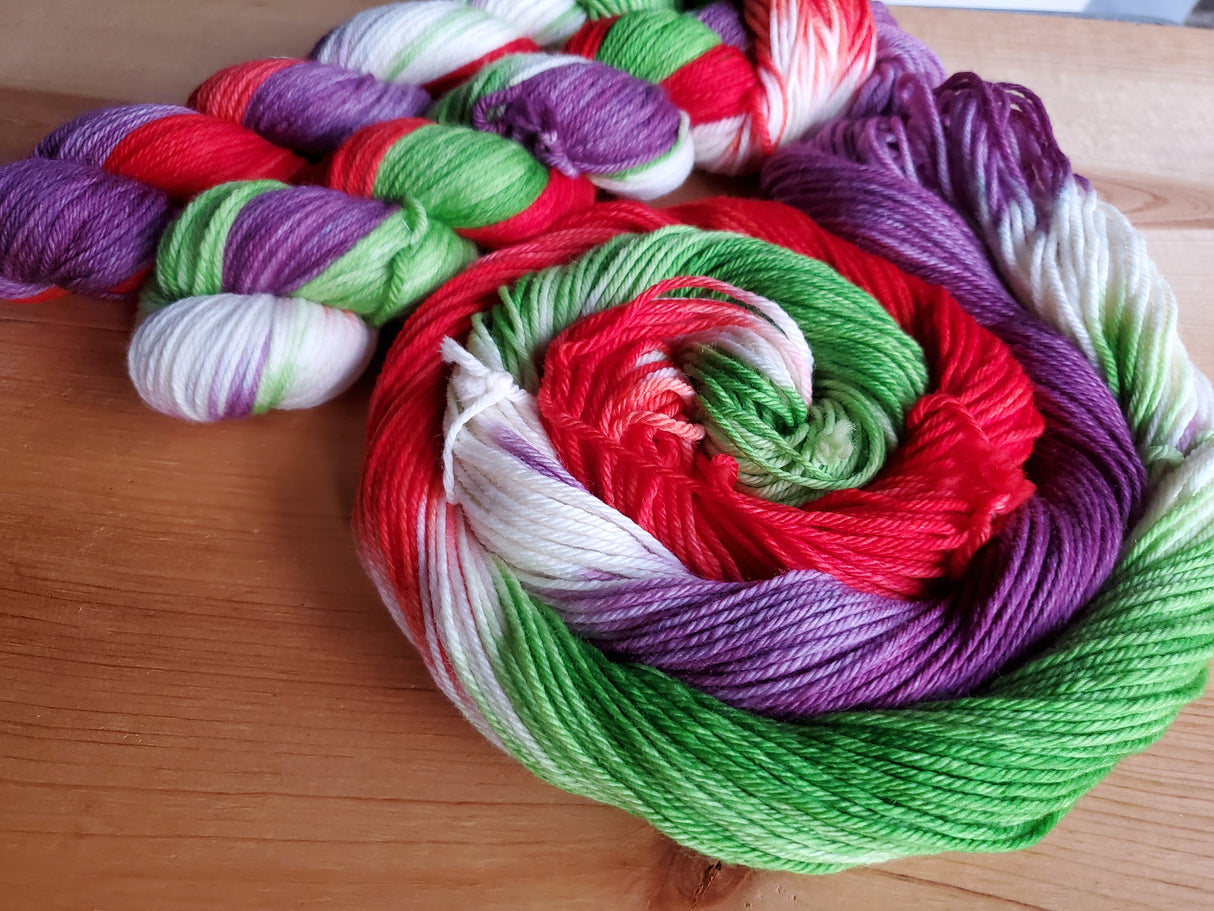 Two skeins snuggle in the upper left corner of the frame beside a swirl of unhanked yarn. The background is a medium toned wood.