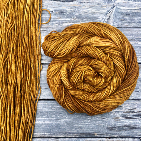 a swath of flat yarn sits on a wooden background with a swirling skein of yarn resting to the right.