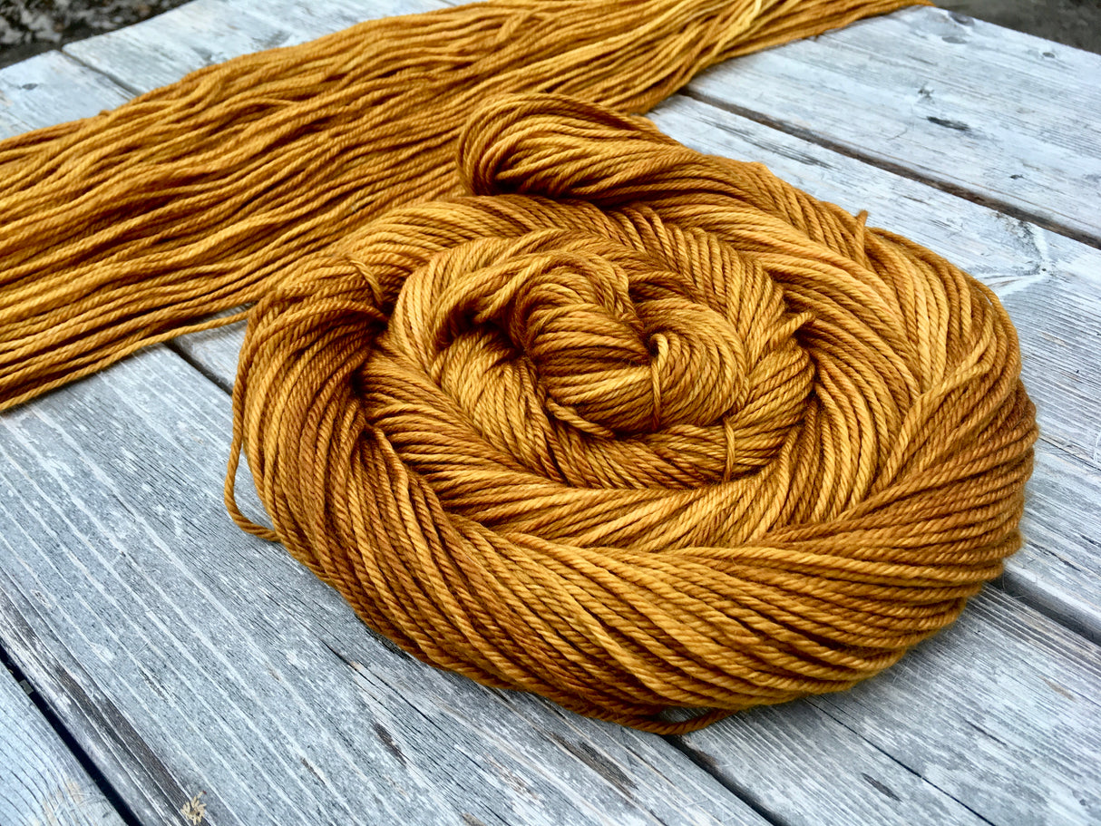 a swath of flat yarn sits on a wooden background with a swirling skein of yarn resting to the right.