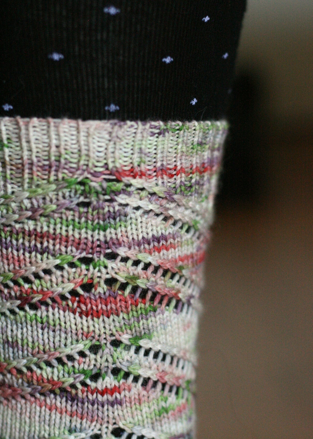 A knitted sock cuff shows off this colorway. The lacy sock is highlighted against black tights with tiny purple stars on them. The background is blurred.
