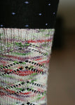 A knitted sock cuff shows off this colorway.  The lacy sock is highlighted against black tights with tiny purple stars on them.  The background is blurred. 