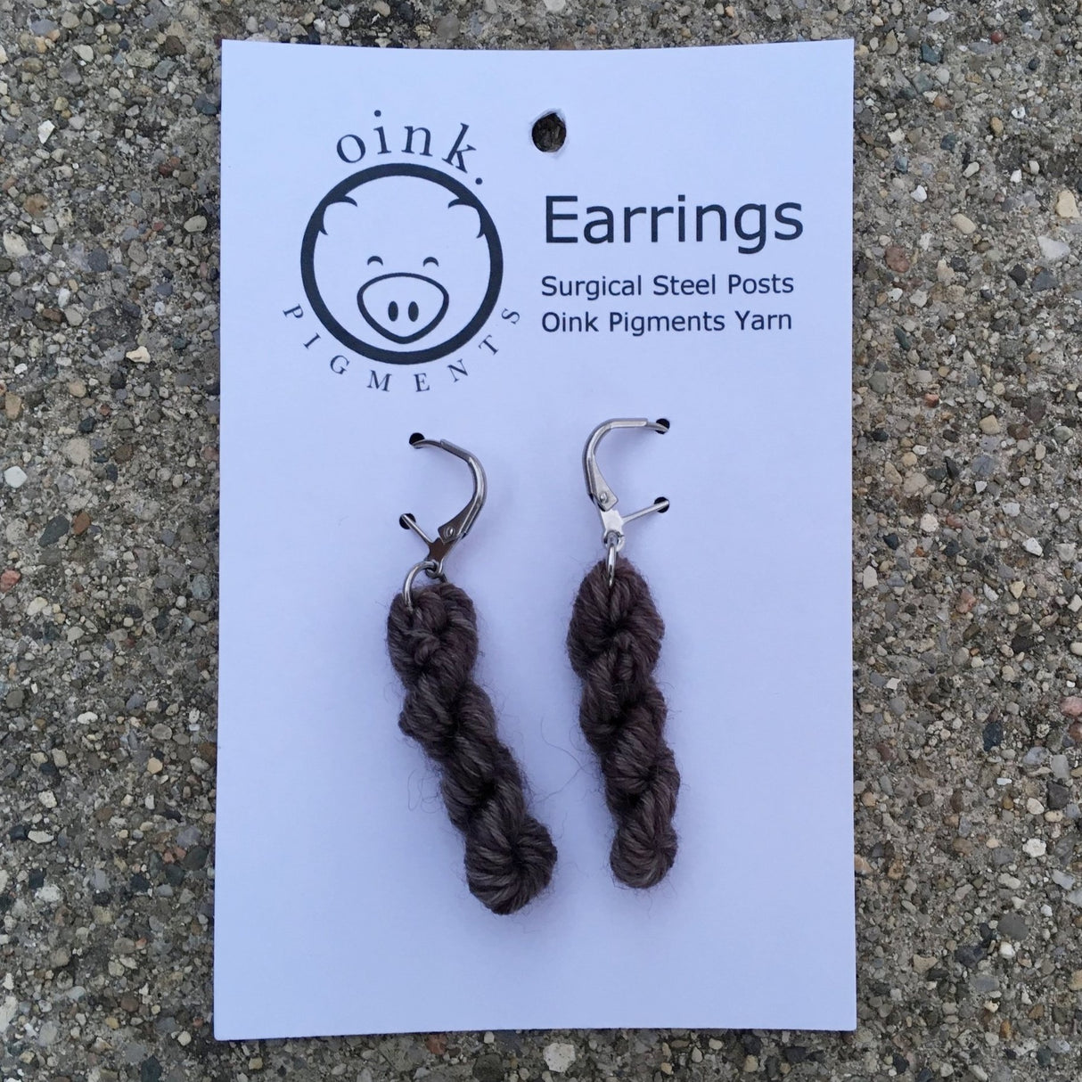 miniature skeins of yarn dangle from steel earring hooks on a white card with the Oink Pigments logo and information at the top.