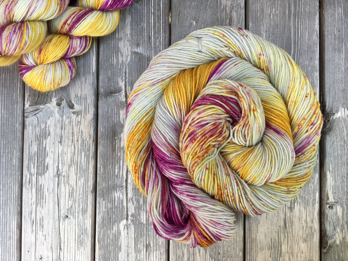 A bright swirl of yarn curls around itself like a labyrinth against a wooden background. Two skeins are peeking out of the upper left corner of the frame.