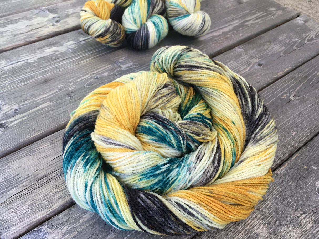 A colorful swirl of yarn curls around itself while three twisted skeins rest in the upper right corner. The yarn is various deep yellow and green tones.