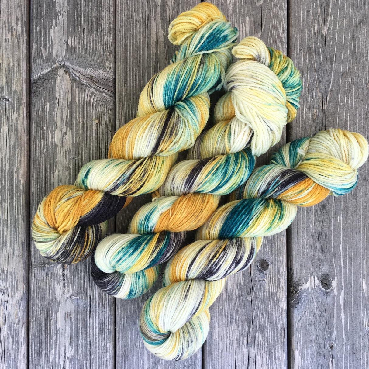 Three twists of yarn rest on a grey wooden backdrop. The yarn is green and yellow with smudges of black.