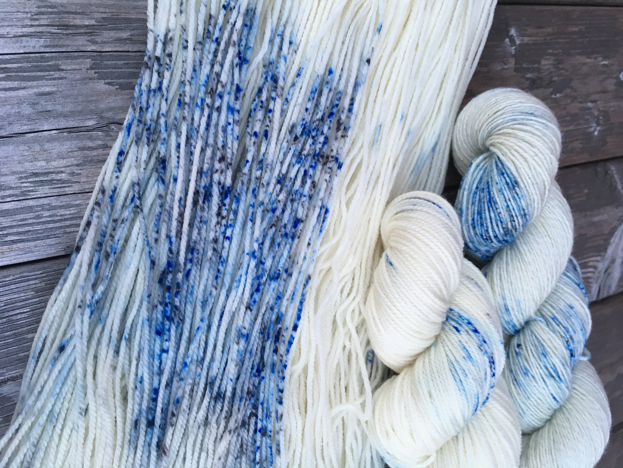 A close up of the speckles featured in this colorway with two twisted hanks resting to the bottom right. The background is grey weathered wood.