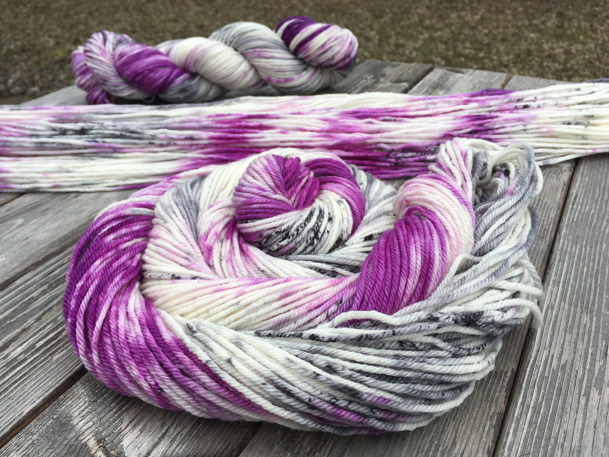 A swirl of yarn rests in the foreground while two more skeins (one laid flat and one twisted) rest in the background. The yarn is sitting on a grey wooden background.