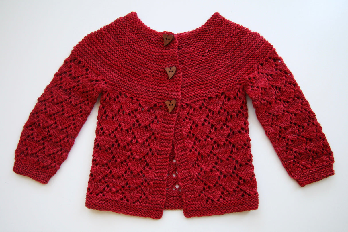 A textured red sweater rests on a clean white background. The yoke of the sweater is garter stitch and the sleeves and body are a delicate heart lace pattern. Three heart shaped buttons complete the sweetness.
