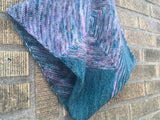 A cowl made of garter triangles rests on a brick wall. 