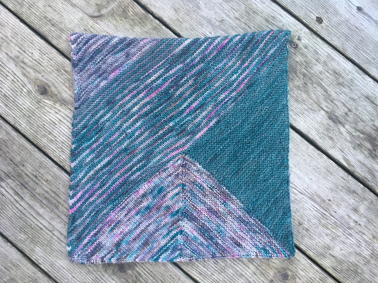 A cowl made of garter triangles in a variety of colors rests on a pale wooden background.