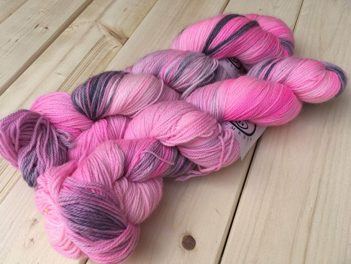 Two skeins of pink and grey yarn rest against a wooden background.