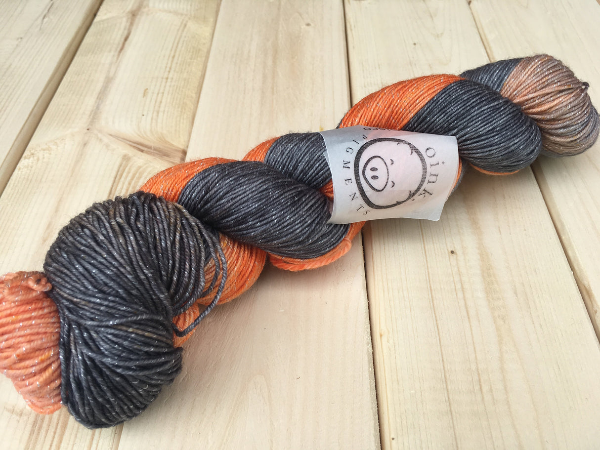 A skein of yarn with subtle sparkles running through it rests diagonally in the frame against a light wooden background.