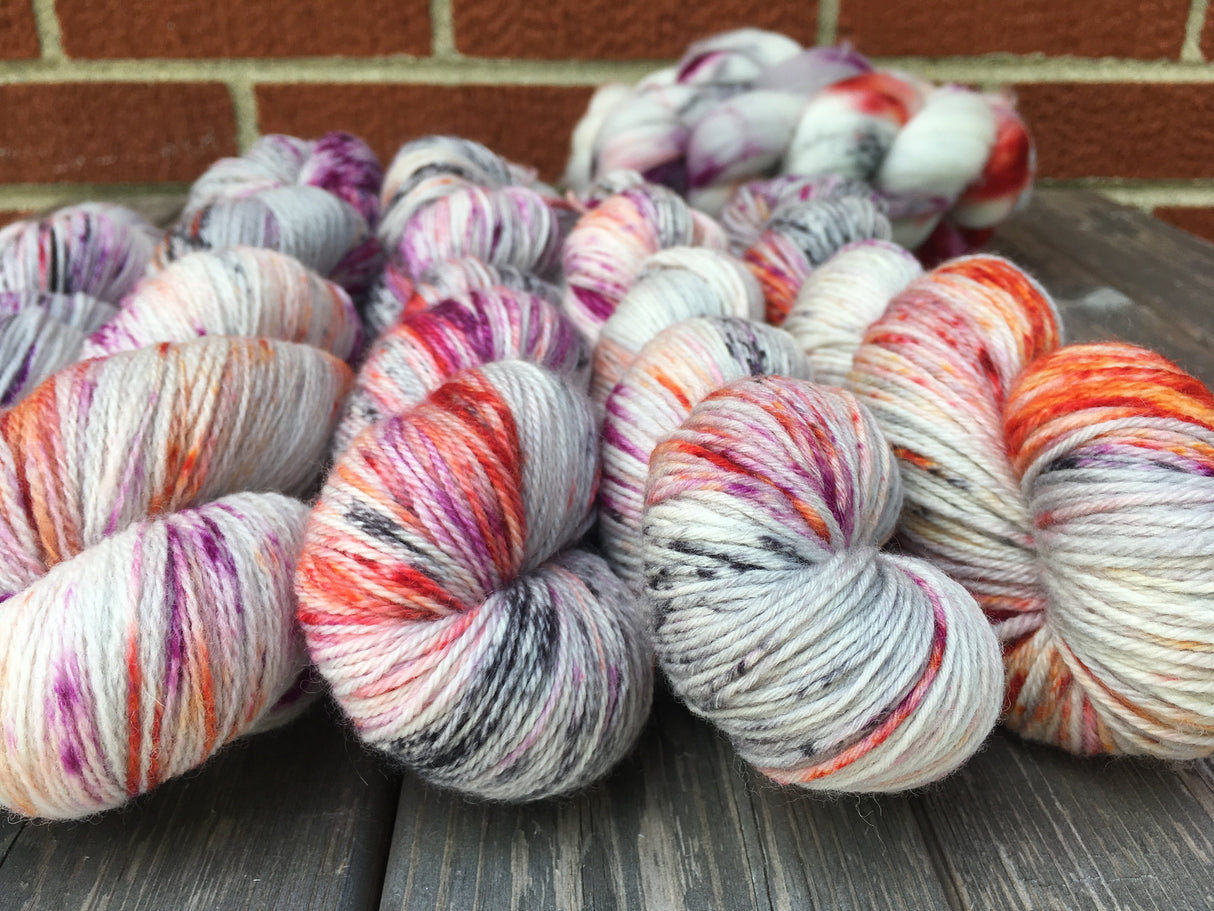 A snuggly bunch of twisted skeins rest on a soft grey wooden surface against a brick background.