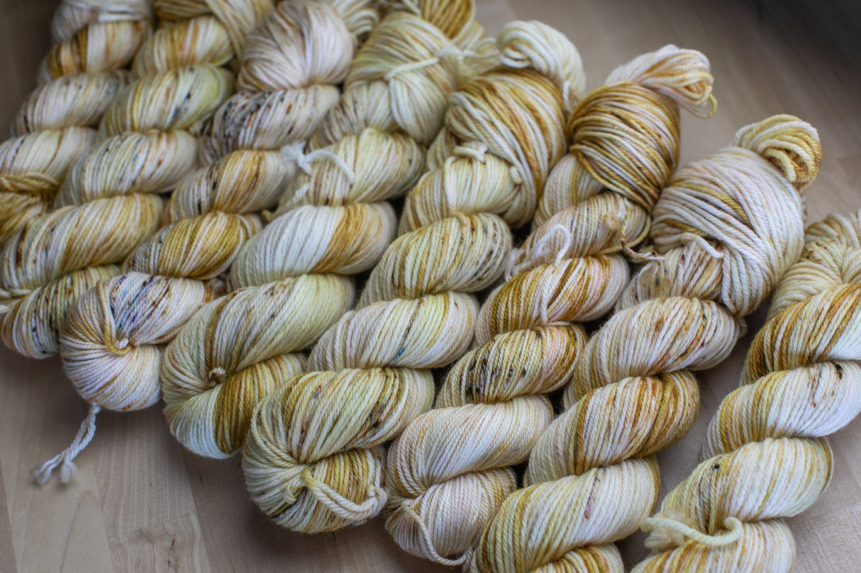 eight glowing skeins of honey-colored and dark speckled yarn snuggle together on a light wooden background.