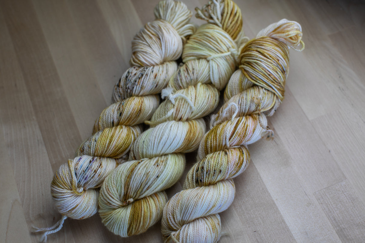 Three skeins of yarn snuggle against a light wooden background.