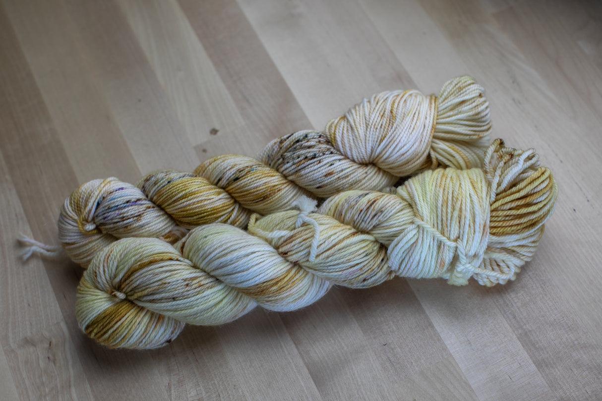Two skeins of speckled and yellow toned yarn rest atop a pale wooden background.