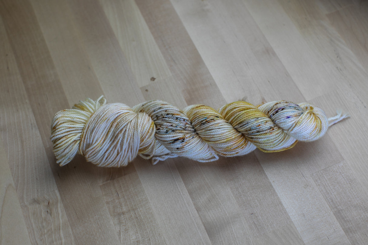 One chubby skein of speckled yarn rests atop a pale wooden background.