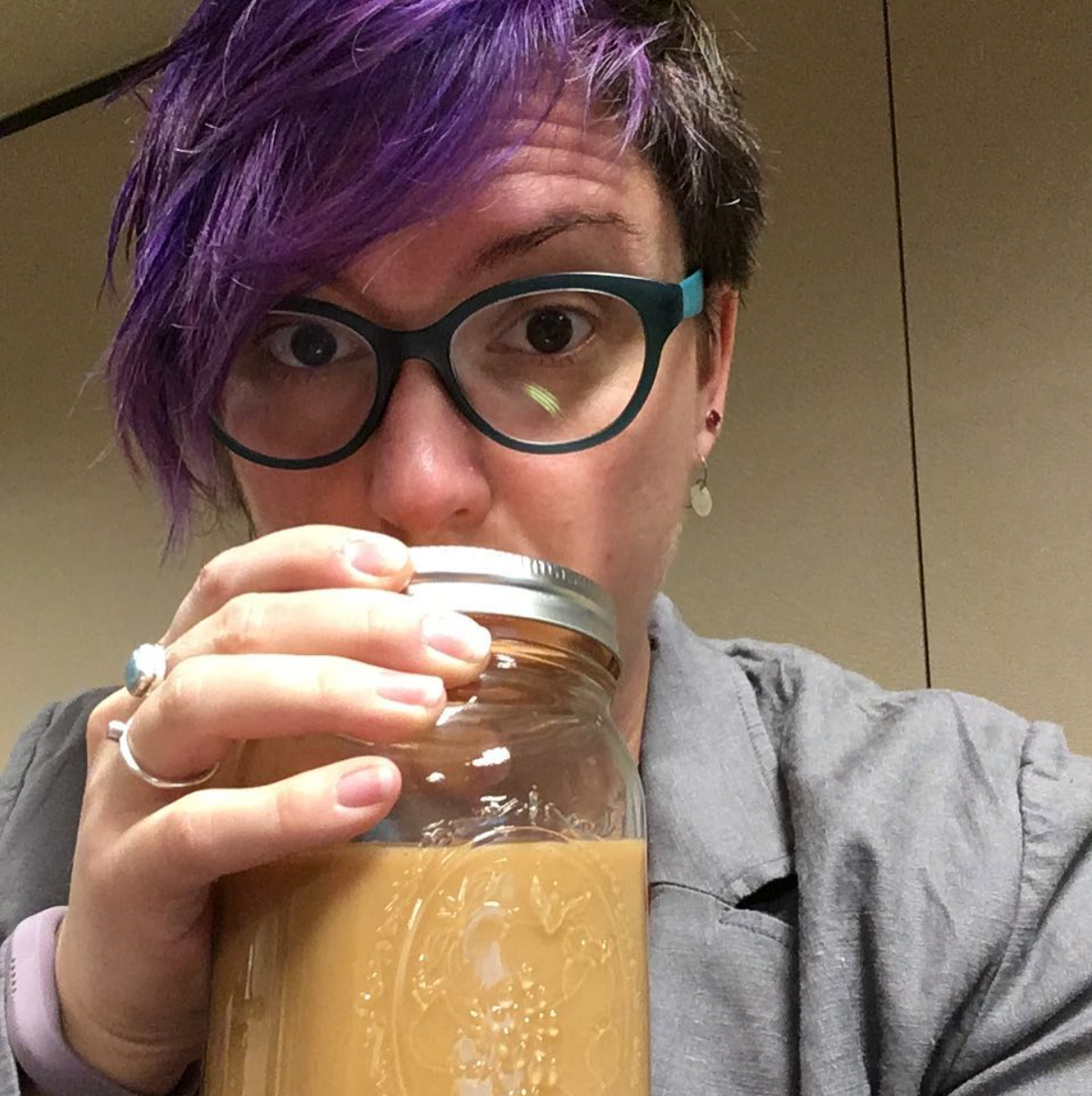 A sweetly sleepy person with purple hair holds a large jar of liquid inspiration.