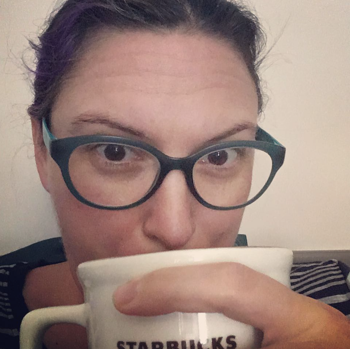 A wonderful bespectacled person sips a comforting beverage from a white mug. The word "starbucks" is partially visible.