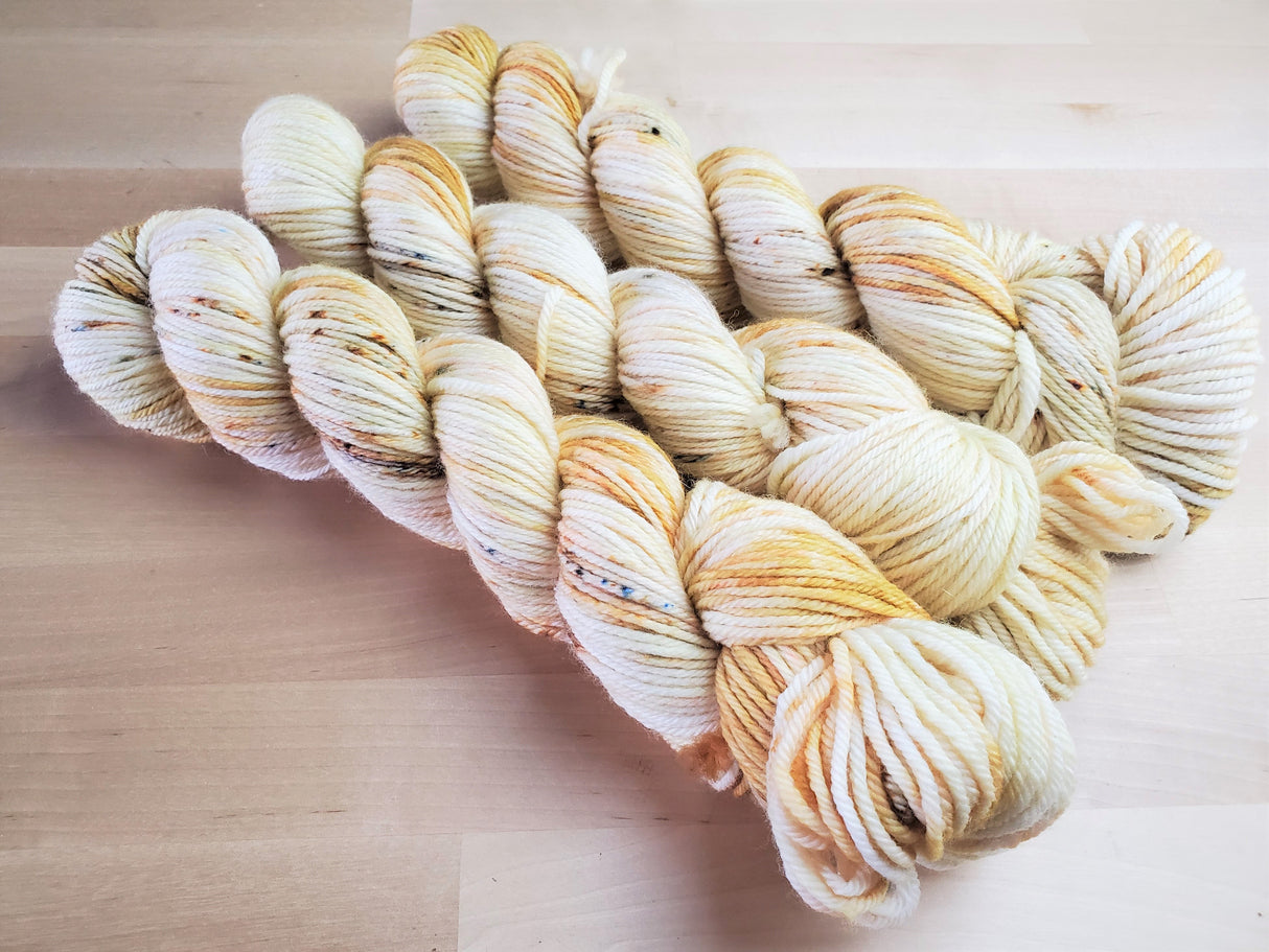 Three twists of pale golden yellow toned yarn rests on a light wooden backdrop.