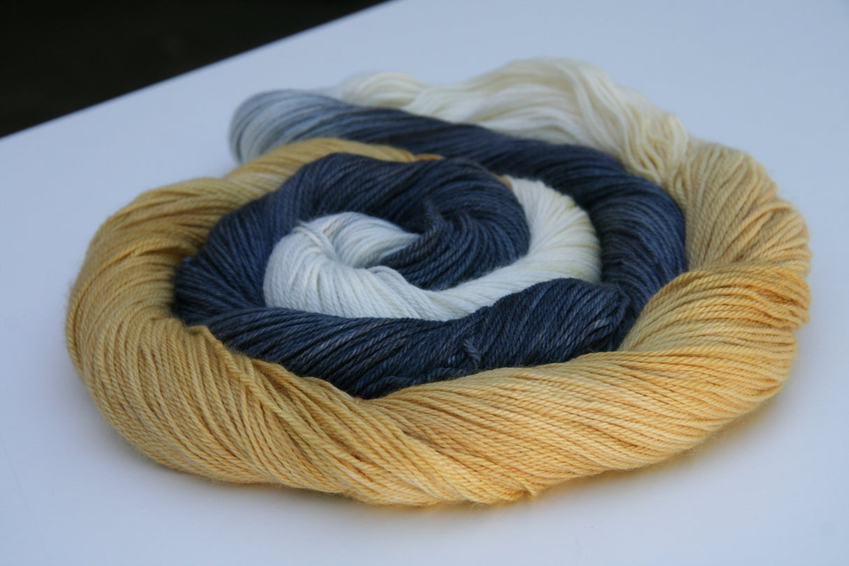 Golden honey yarn curls around a darker charcoal grey and white as it rests against a clean white background.
