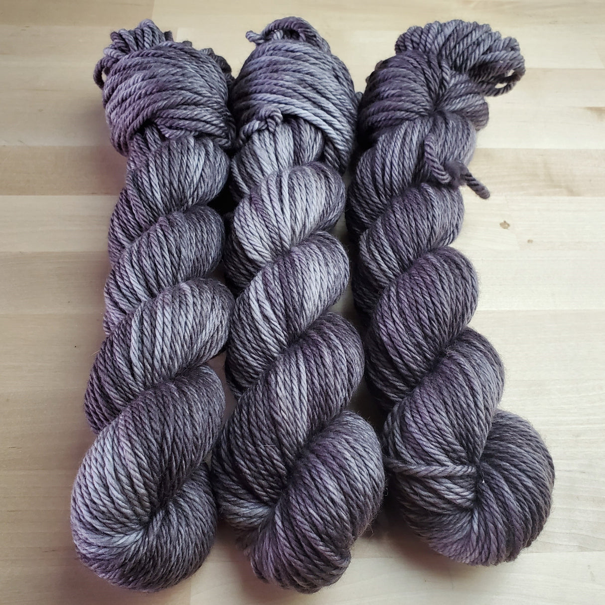 Three skeins of yarn snuggle against a light wooden background.