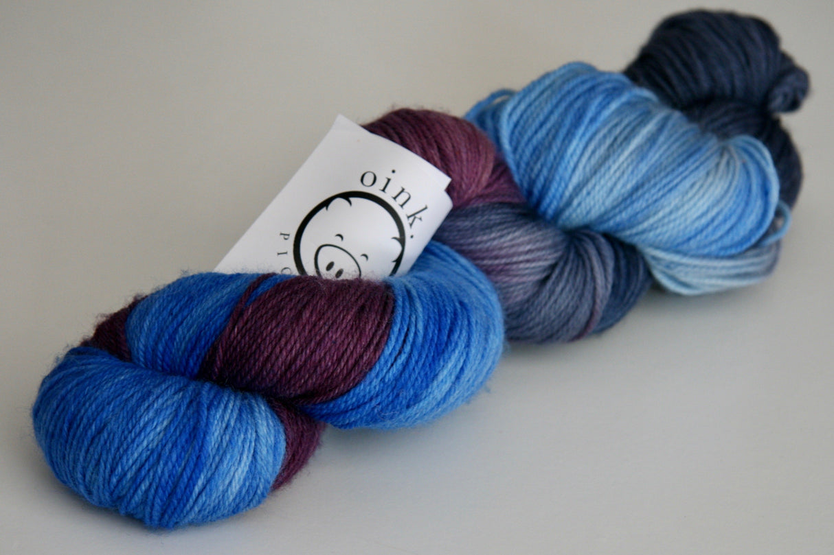 a plump skein of blue, purple, and soft grey yarn rests on a clean white background.