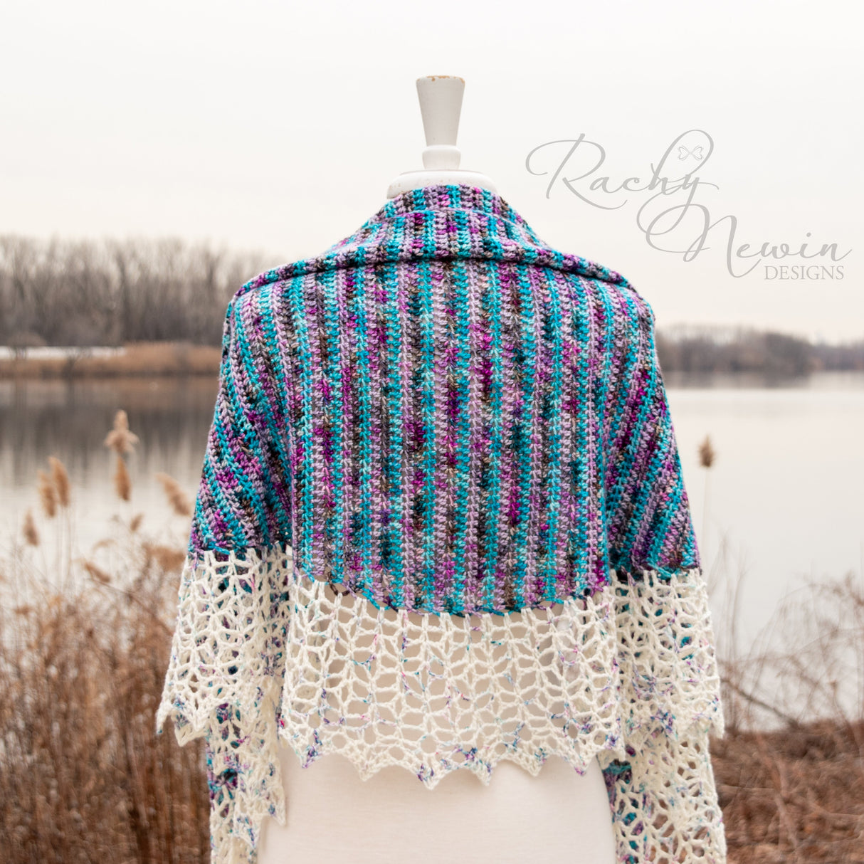 A beautiful shawl with strong vertical ridges and a delicate cream crocheted lace rests on a mannequin in a restful lakeside location.