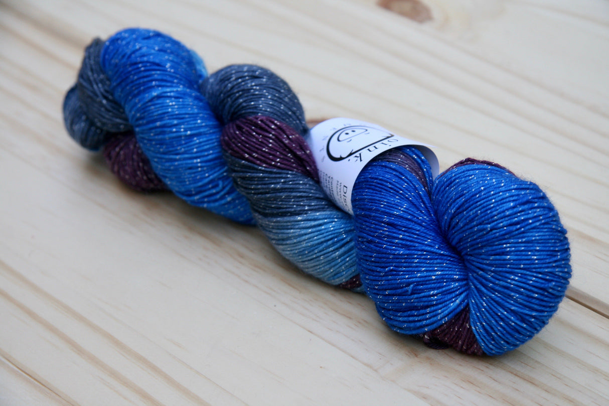 A rich blue skein of yarn with tiny silvery sparkles rests on a pale wooden background.