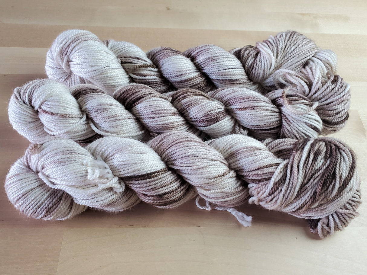 Three skeins of yarn snuggle against a light wooden background.