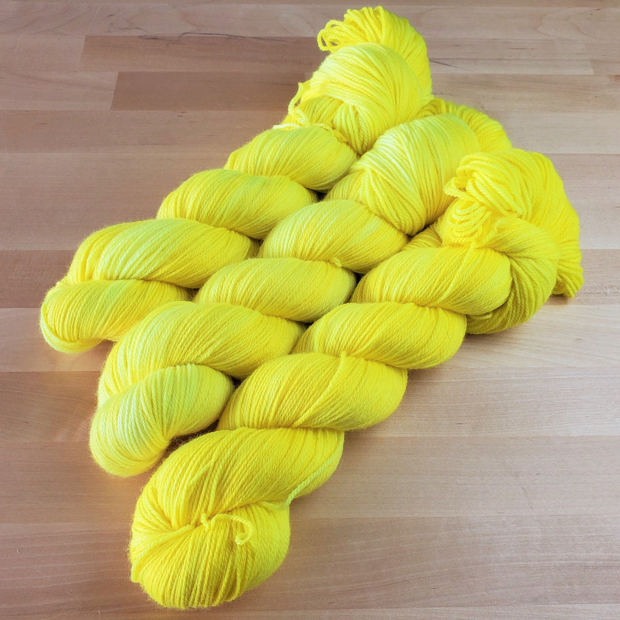 Three skeins of yarn snuggle against a light wooden background.