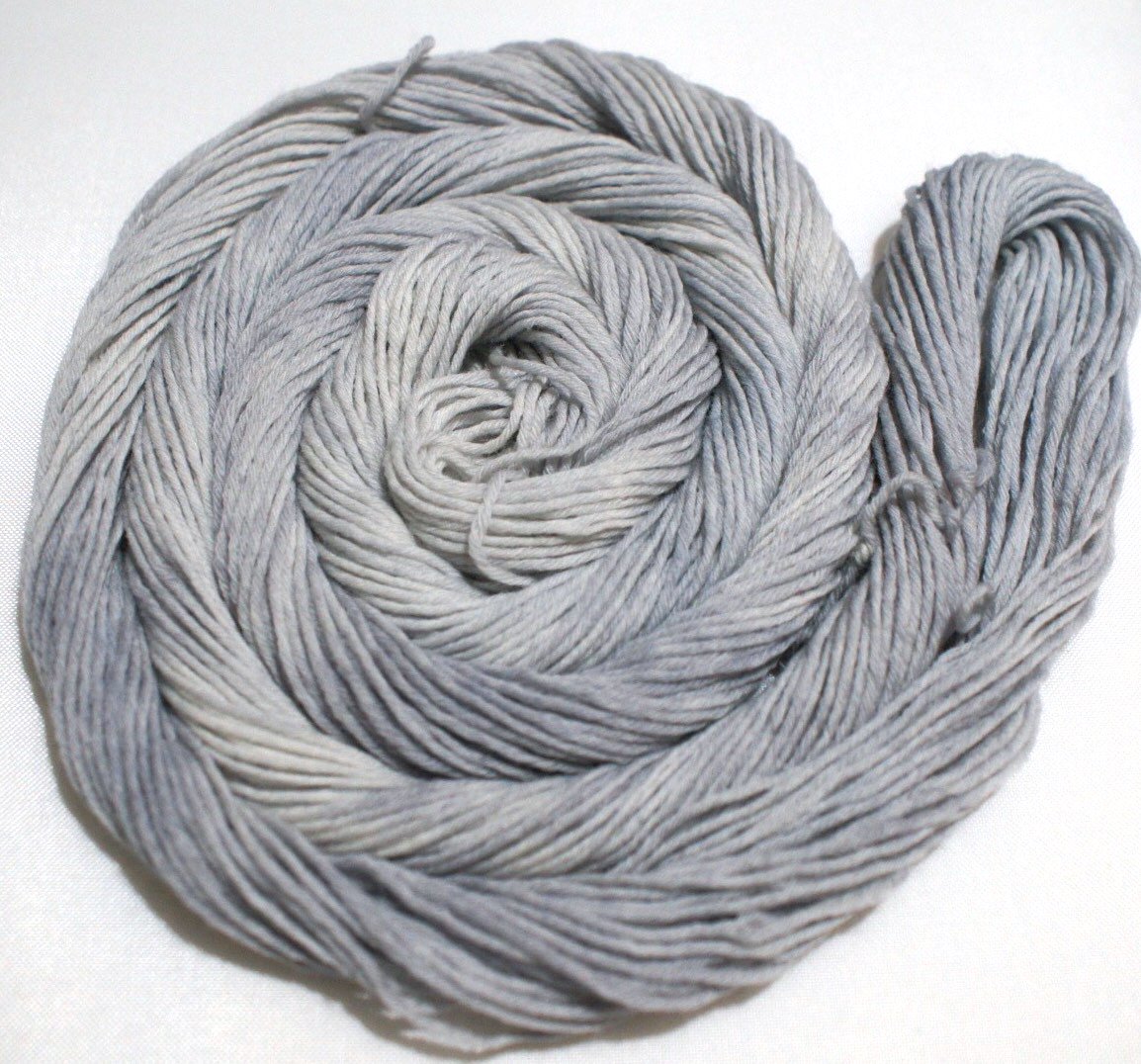 A soft grey swirl of yarn curls around itself like a labyrinth against a white background.