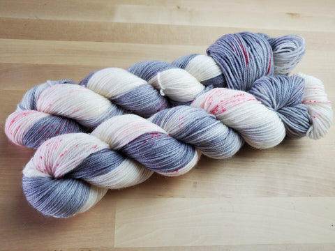 Two skeins of yarn rest diagonally in the frame against a wooden background. 4-Play colorway in disco base.