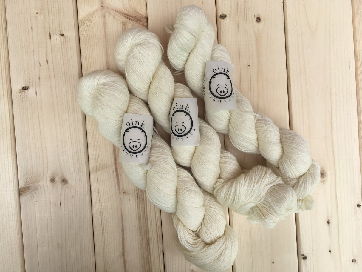 Three skeins lie against a pale wooden background.