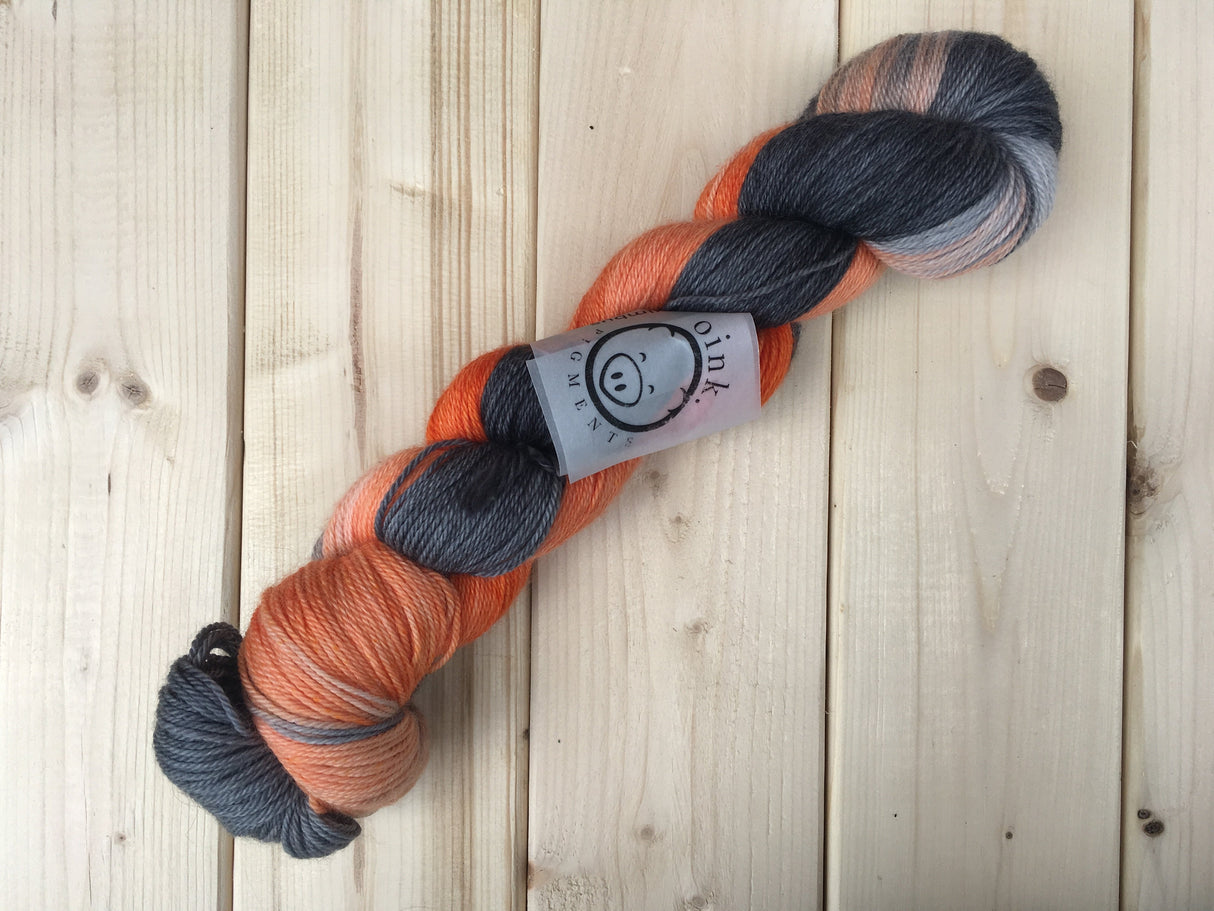 A twisted skein of orange and black-grey yarn lies against a light wooden background.