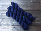Three skeins of yarn rest dramatically on a wooden background.