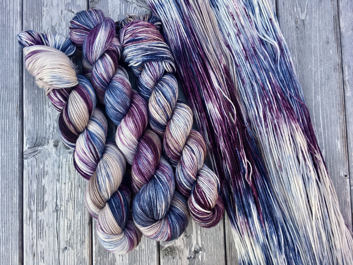 Three skeins lie in twists to the left, beside a swath of yarn resting against a grey wooden background.