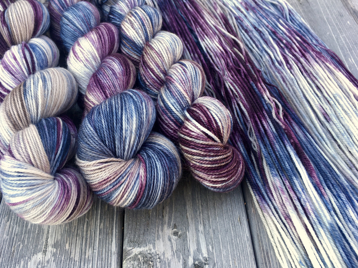 Three skeins lie in twists to the left, beside a swath of yarn resting against a grey wooden background.