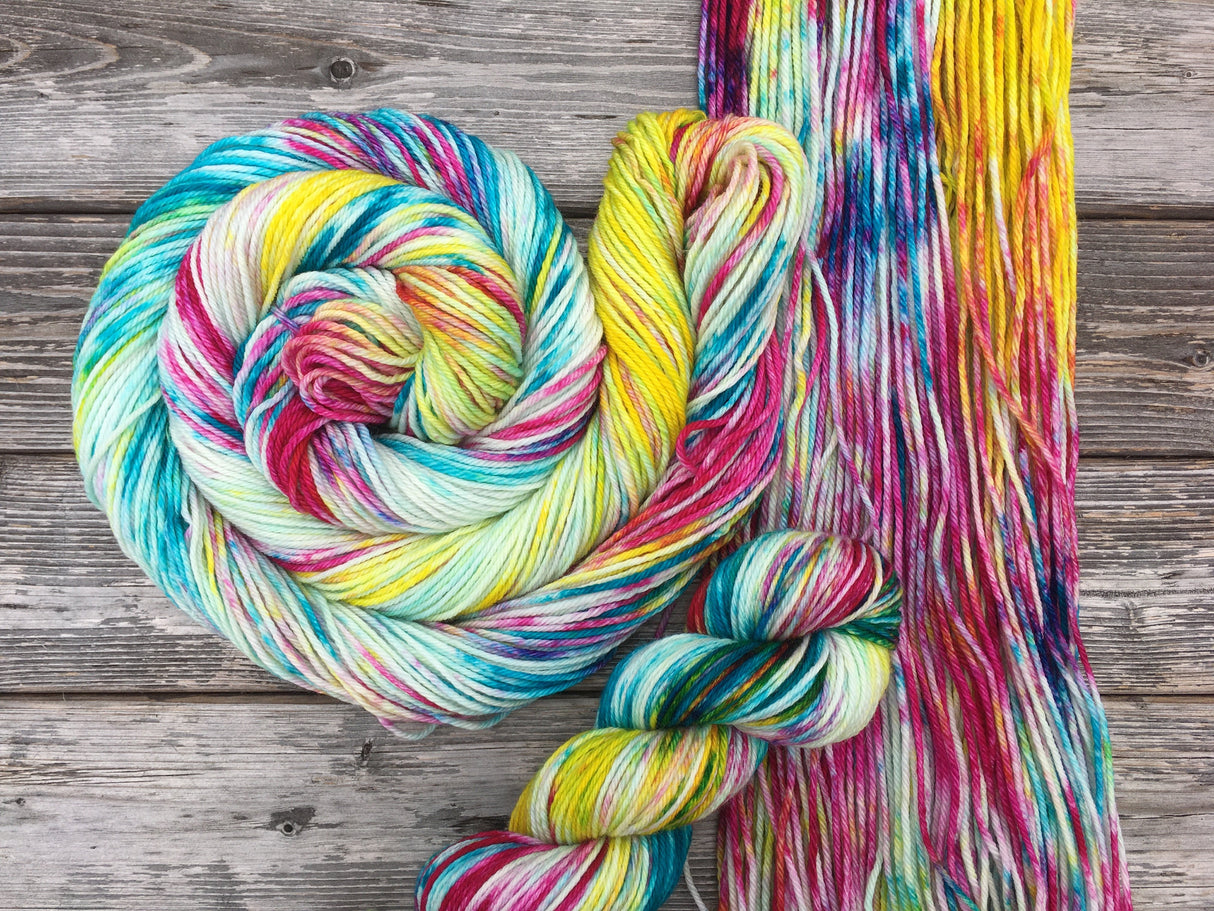A colorful swirl of yarn curls around it self atop an untwisted hank of yarn. A single skein rests near the bottom of the frame.