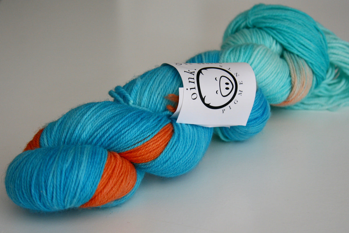 a single twisted skein of yarn rests on a clean white background. The white Oink Pigments label is visible about halfway down the skein.