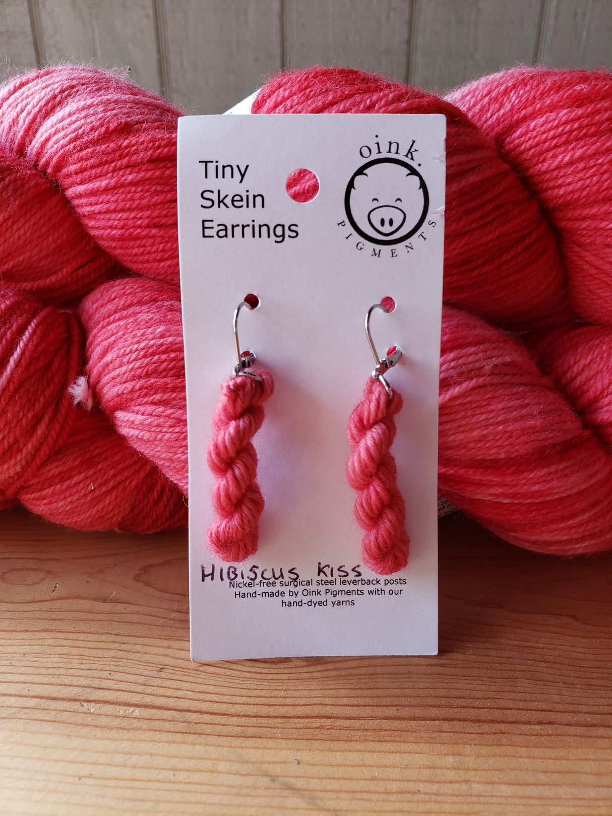 A card with two miniature skeins rests against full size skeins of wool on a wooden tabletop.