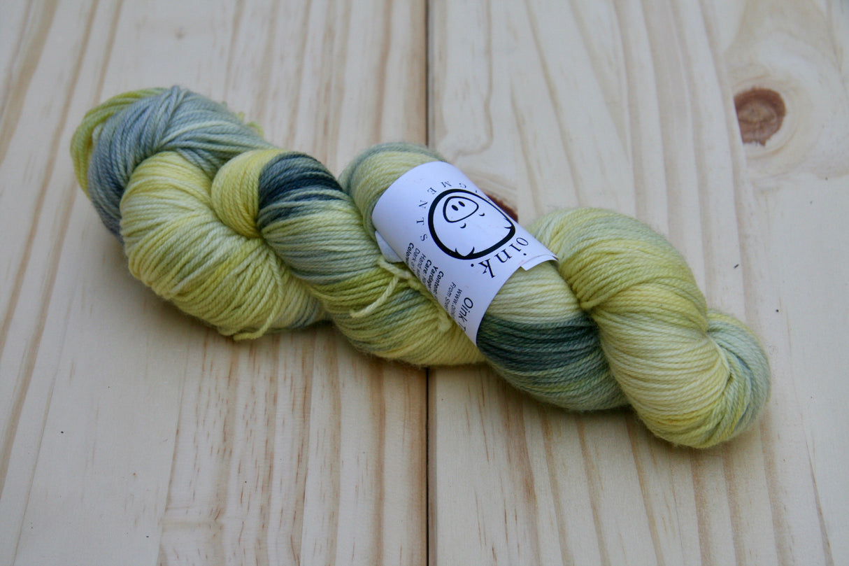 A twisted skein of lemony yellow, black, and grey rests against a pale wooden background.