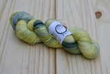 A twisted skein of lemony yellow, black, and grey rests against a pale wooden background. 