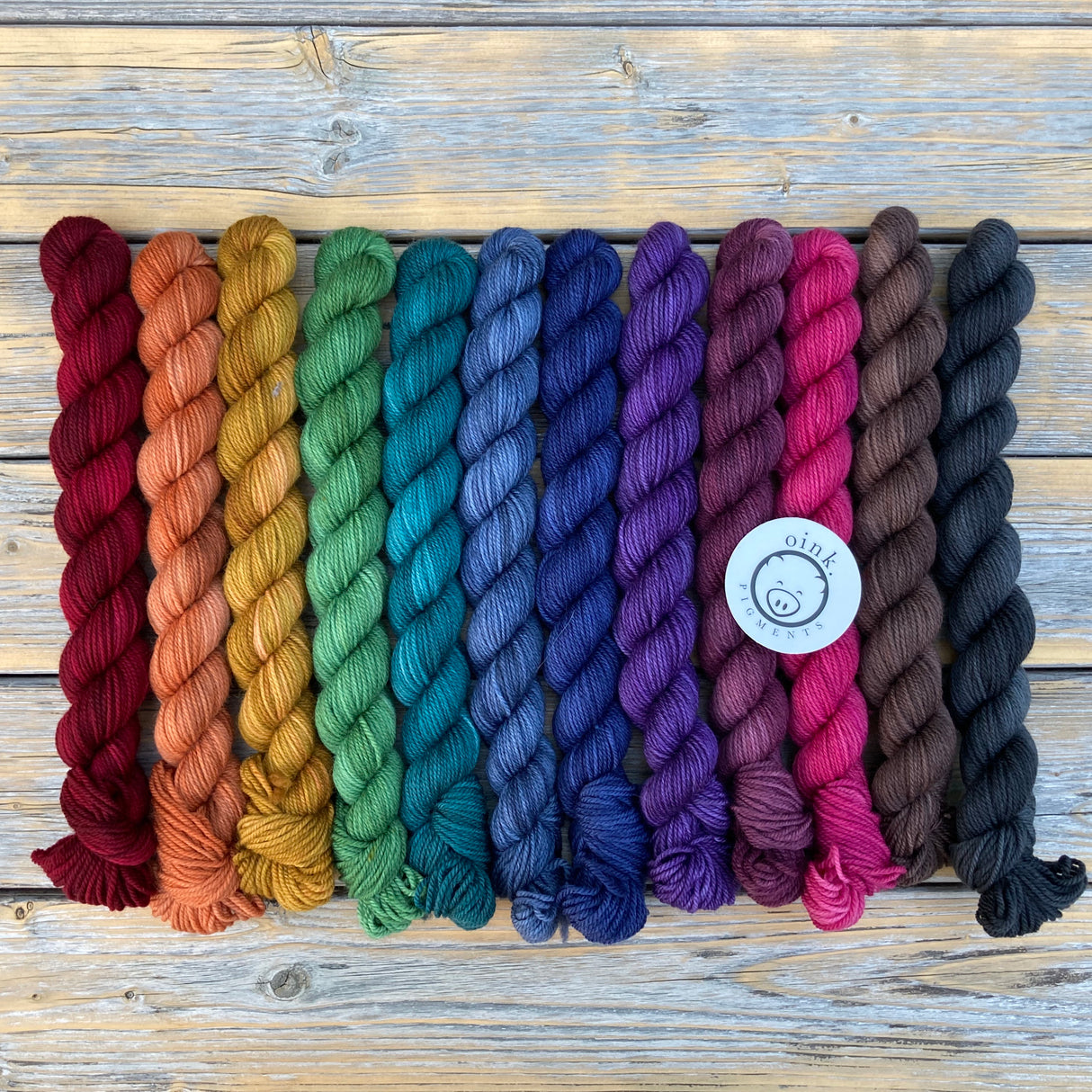 A dark rainbow of small skeins rests on a wooden background
