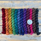 A dark rainbow of small skeins rests on a wooden background