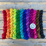 A bright rainbow of small skeins rests on a wooden background.