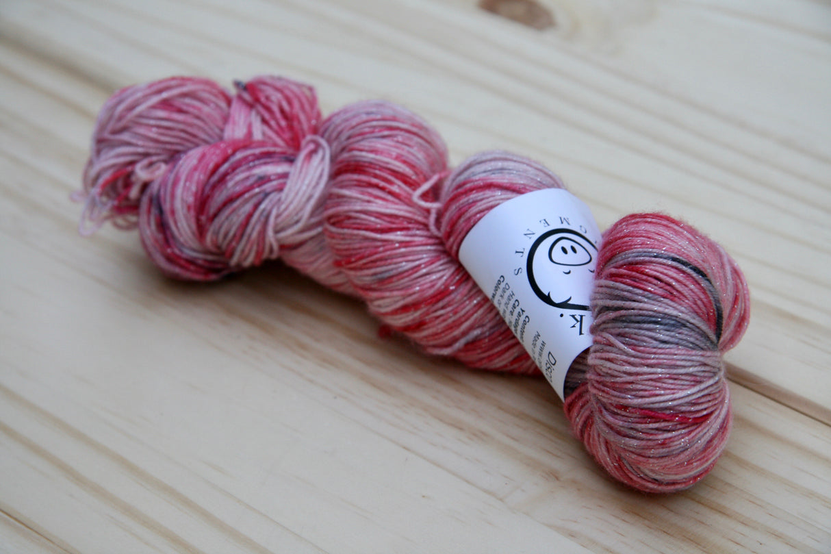 a sparkly skein of yarn in reds, cream, and black rests on a light wooden background.
