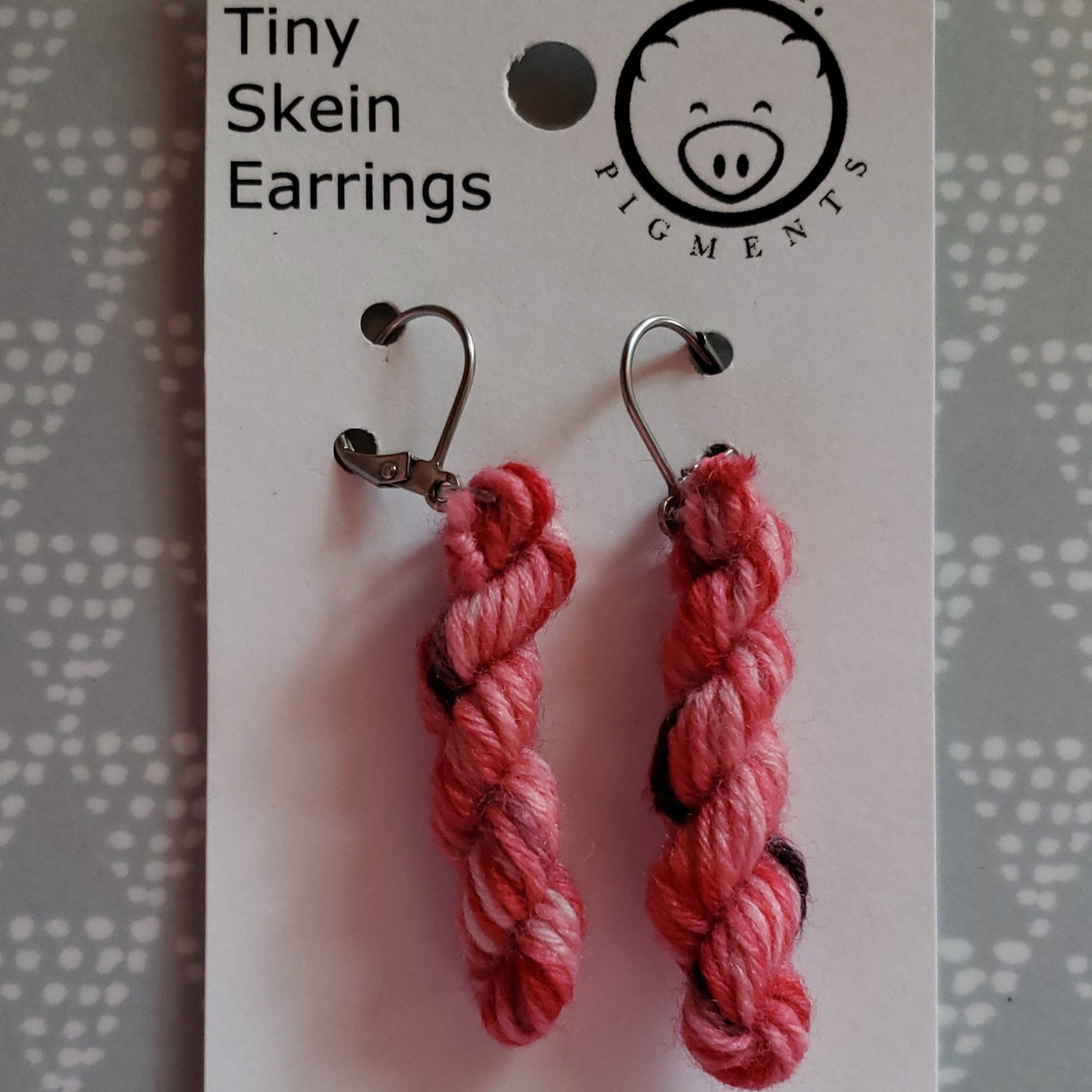 two mini skeins of yarn dangle from earwires against a white card. The oink logo is at the top right.